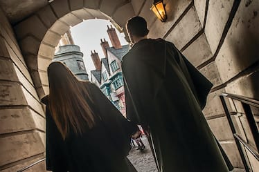 A couple wearing wizard robes walks hand in hand towards Diagon Alley inside Universal Orlando Studios Orlando.